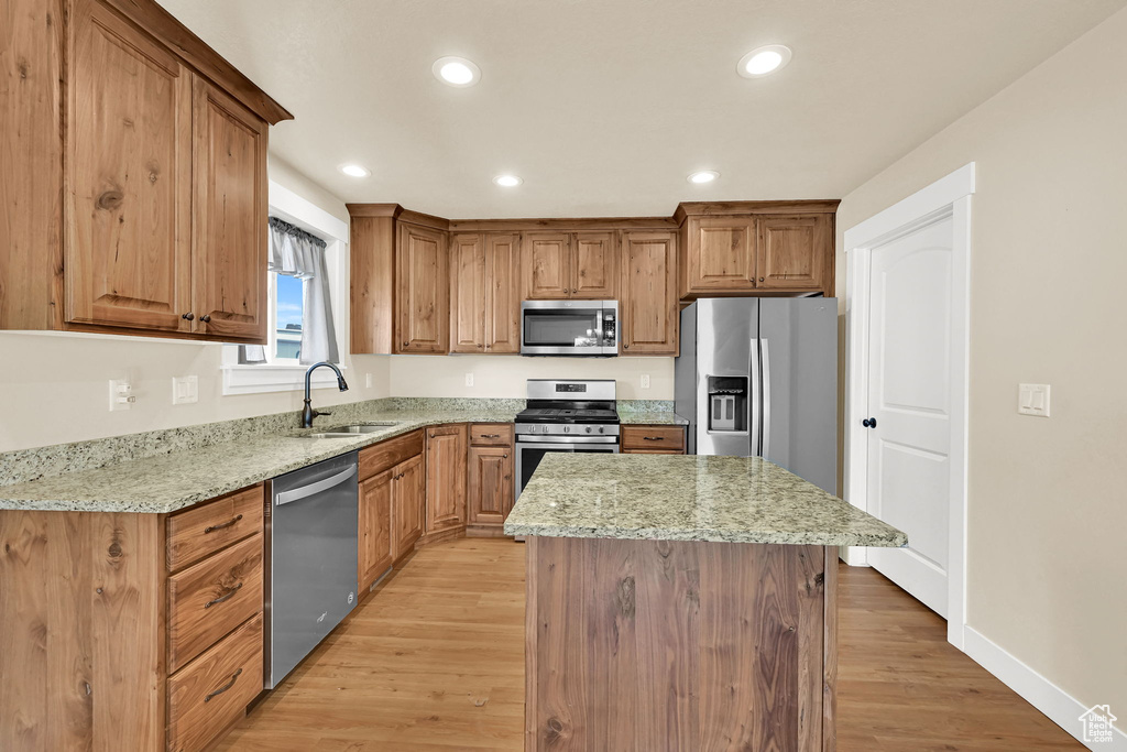 Kitchen with appliances with stainless steel finishes, light stone counters, a kitchen island, light wood-style floors, and recessed lighting