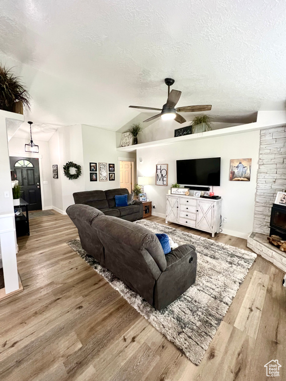 Living area featuring ceiling fan, a textured ceiling, wood finished floors, lofted ceiling, and a wood stove
