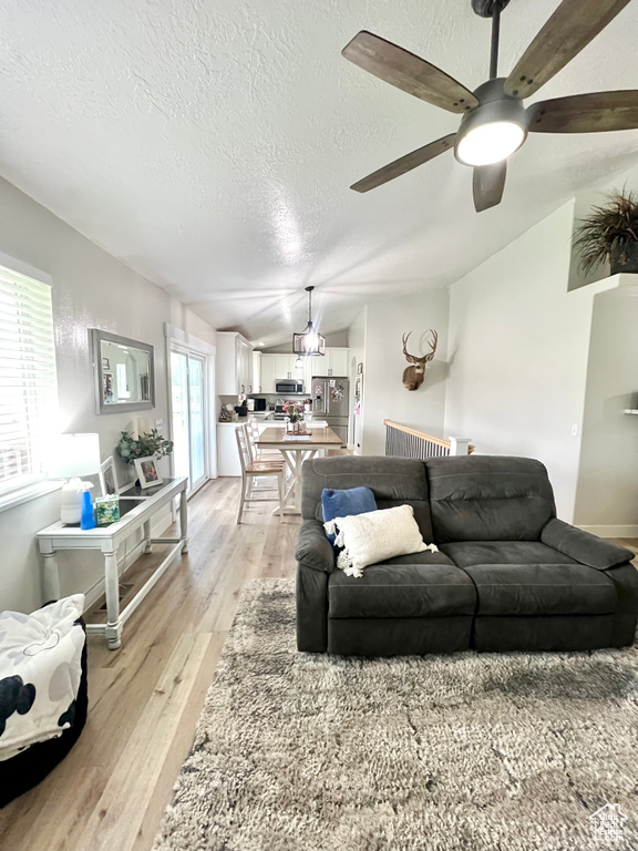 Living room with lofted ceiling, ceiling fan, a textured ceiling, and light wood-type flooring