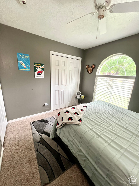 Carpeted bedroom with a closet, a textured ceiling, and a ceiling fan