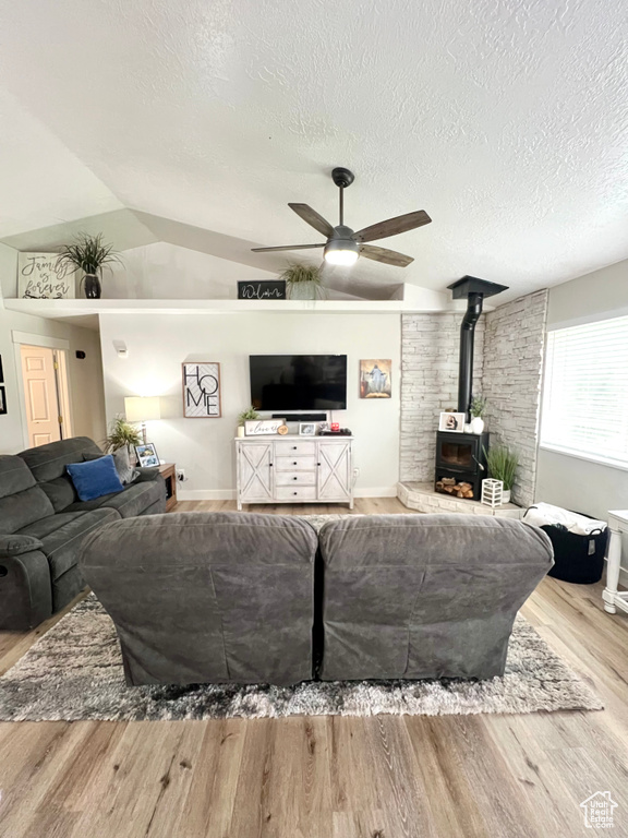 Living area featuring a ceiling fan, a wood stove, wood finished floors, a textured ceiling, and lofted ceiling