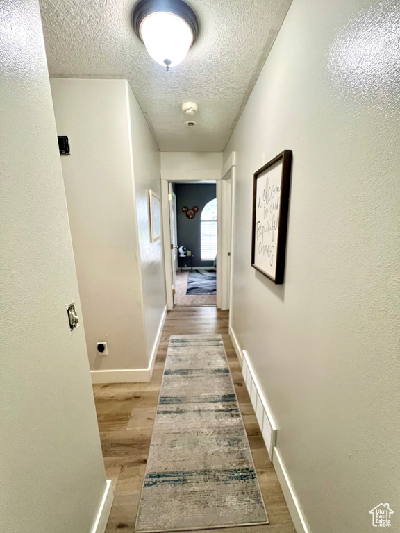 Corridor with a textured ceiling and light wood-style flooring