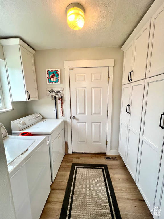 Laundry area featuring cabinet space, washer and clothes dryer, light wood-type flooring, and a textured ceiling