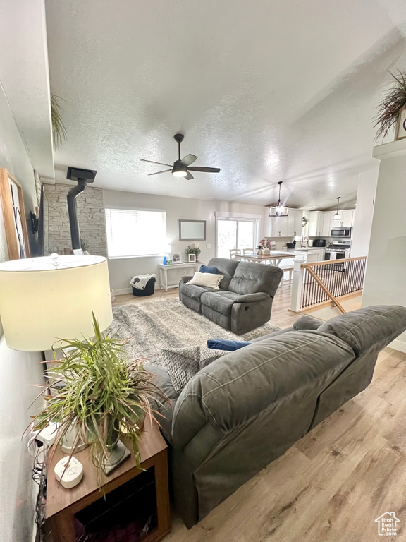 Living area featuring light wood-style flooring, ceiling fan, a wood stove, and a textured ceiling