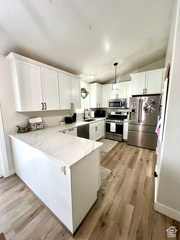 Kitchen with appliances with stainless steel finishes, a peninsula, light wood-style flooring, and lofted ceiling