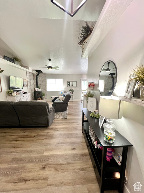 Living room with a wood stove, light wood-style flooring, and a ceiling fan