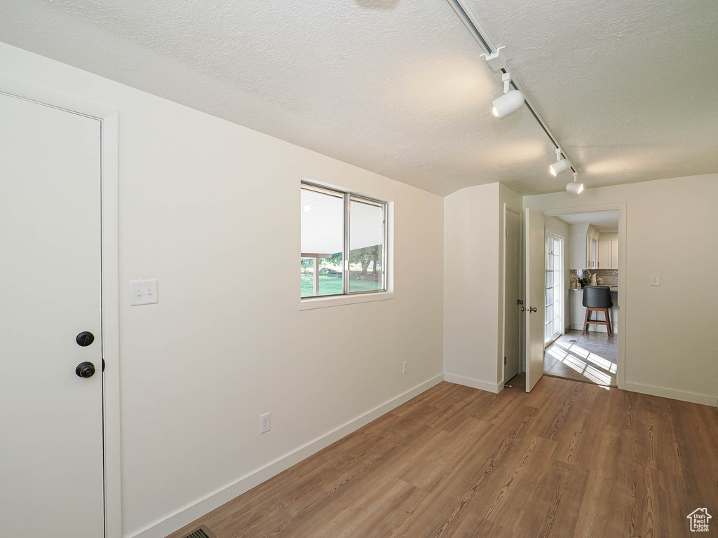 Unfurnished room featuring a textured ceiling, track lighting, and wood finished floors