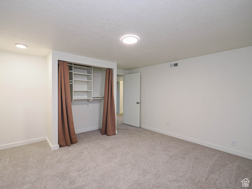 Unfurnished bedroom with light colored carpet, a textured ceiling, and a closet