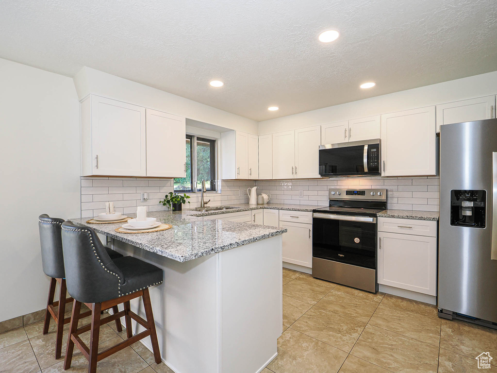 Kitchen featuring stainless steel appliances, a peninsula, white cabinetry, decorative backsplash, and a textured ceiling