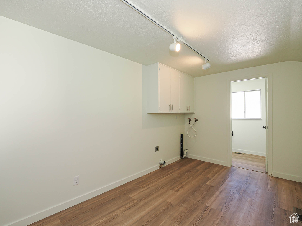Laundry area featuring cabinet space, a textured ceiling, wood finished floors, hookup for an electric dryer, and rail lighting