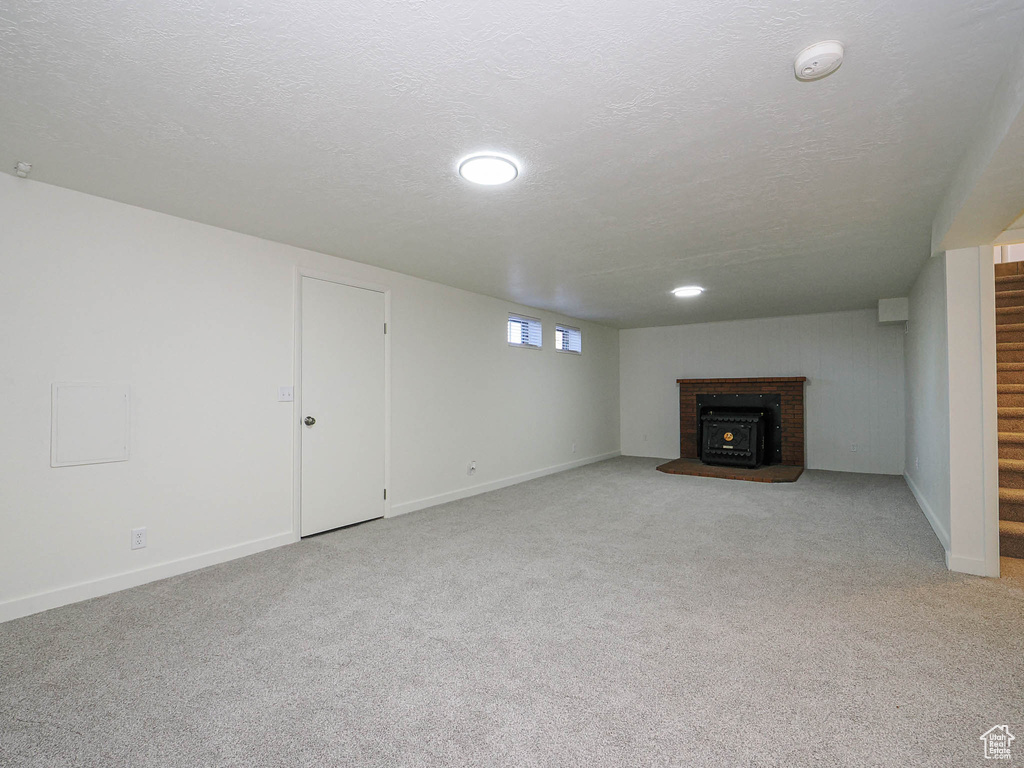 Unfurnished living room featuring stairs, light colored carpet, a brick fireplace, and a textured ceiling