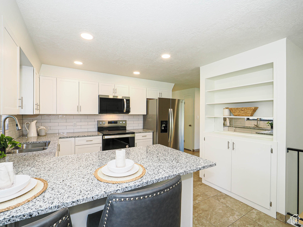Kitchen featuring appliances with stainless steel finishes, a breakfast bar, light stone counters, a textured ceiling, and a peninsula