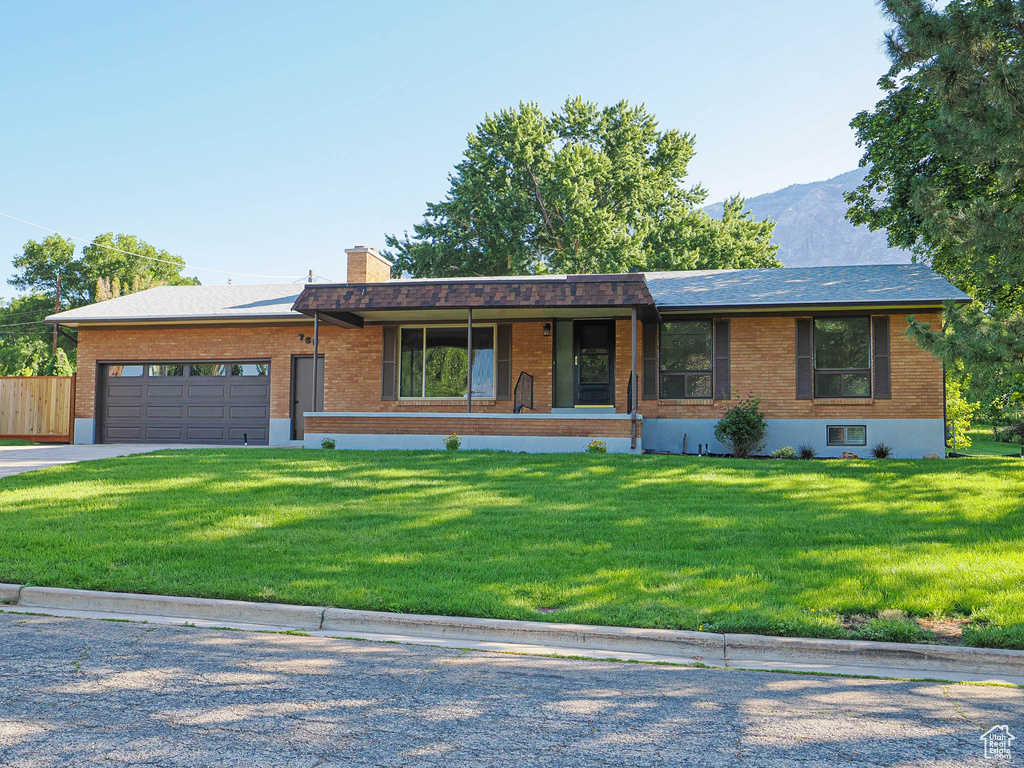 Ranch-style house with brick siding, a garage, a front lawn, a chimney, and driveway
