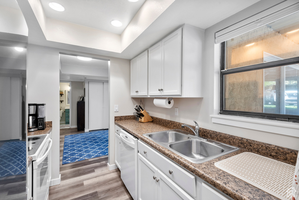 Kitchen featuring white appliances, light wood-type flooring, white cabinets, a tray ceiling, and recessed lighting