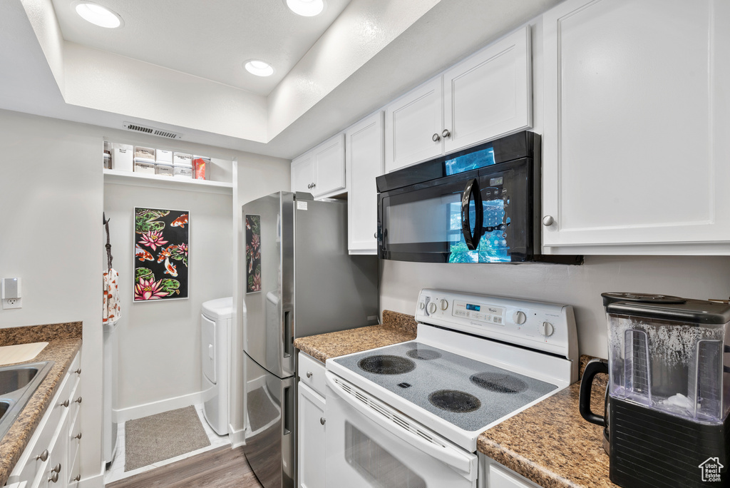 Kitchen featuring white electric stove, black microwave, wood finished floors, white cabinets, and recessed lighting