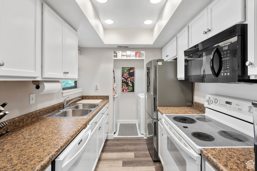 Kitchen featuring white appliances, white cabinets, wood finished floors, a raised ceiling, and recessed lighting