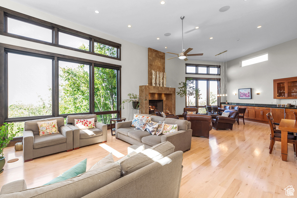 Living area featuring a high ceiling, ceiling fan, a fireplace, light wood-type flooring, and recessed lighting