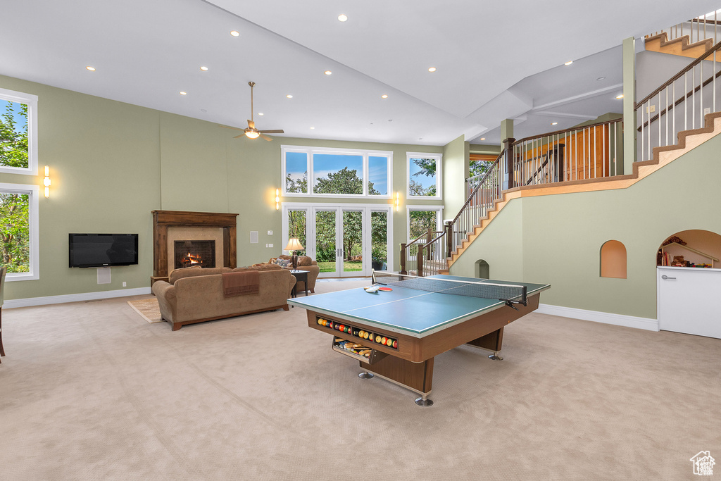 Rec room featuring a towering ceiling, a ceiling fan, carpet floors, a warm lit fireplace, and recessed lighting