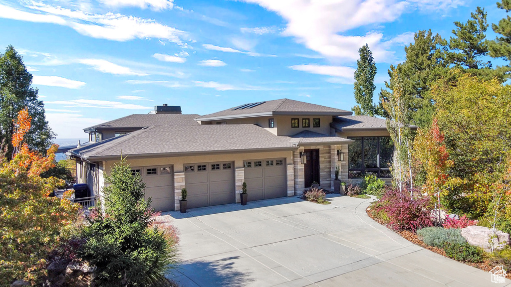 Prairie-style house with an attached garage, concrete driveway, solar panels, stone siding, and a chimney