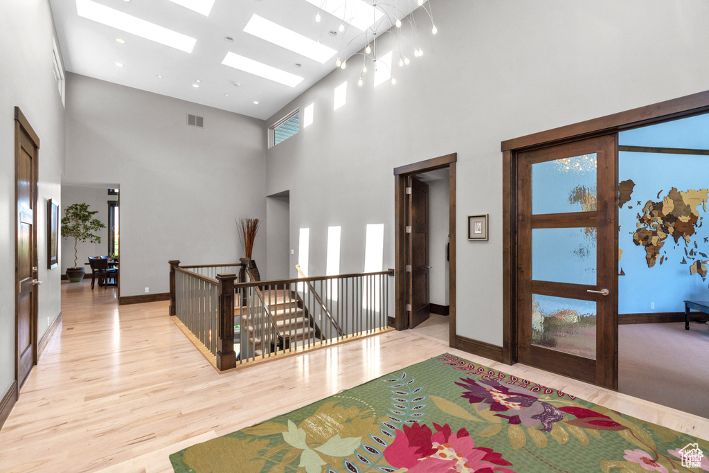 Corridor with an upstairs landing, a towering ceiling, light wood finished floors, and a skylight