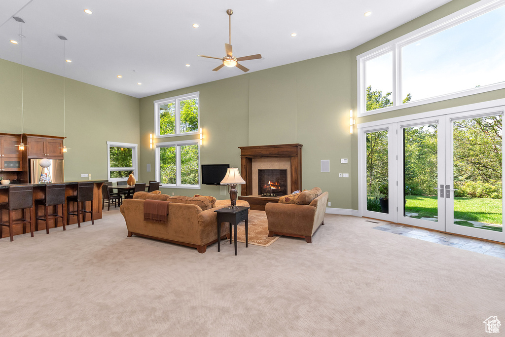 Living area with a towering ceiling, light carpet, a lit fireplace, recessed lighting, and ceiling fan