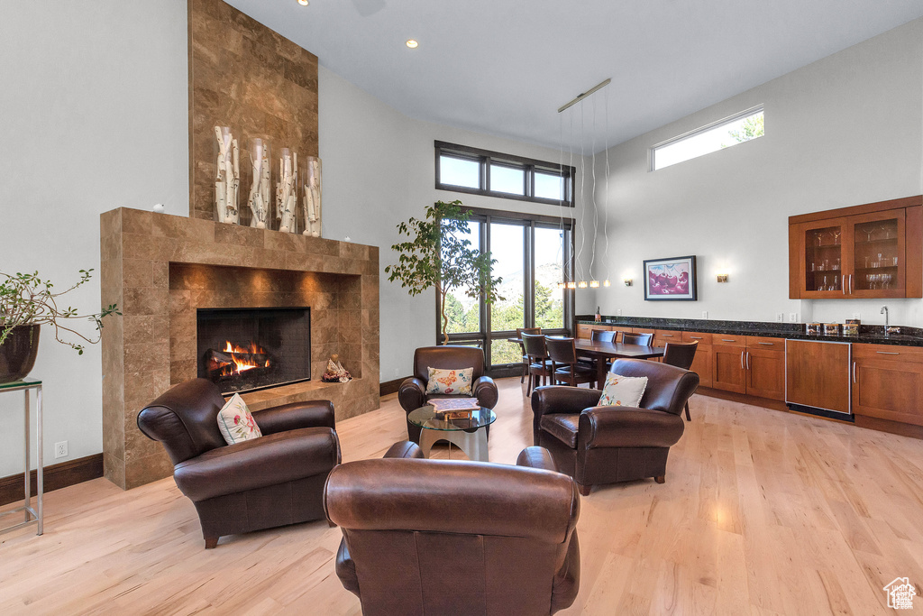 Living area with a high ceiling, light wood-type flooring, a fireplace, plenty of natural light, and bar area