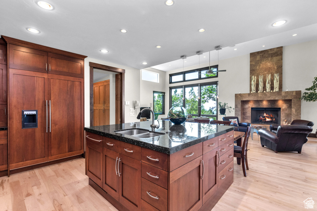 Kitchen with light wood finished floors, a large fireplace, paneled built in refrigerator, recessed lighting, and dark stone counters