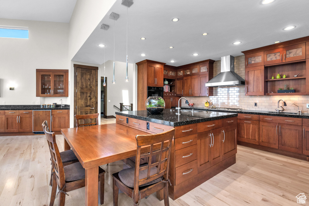 Kitchen with wall chimney exhaust hood, open shelves, a kitchen island with sink, light wood-style flooring, and recessed lighting