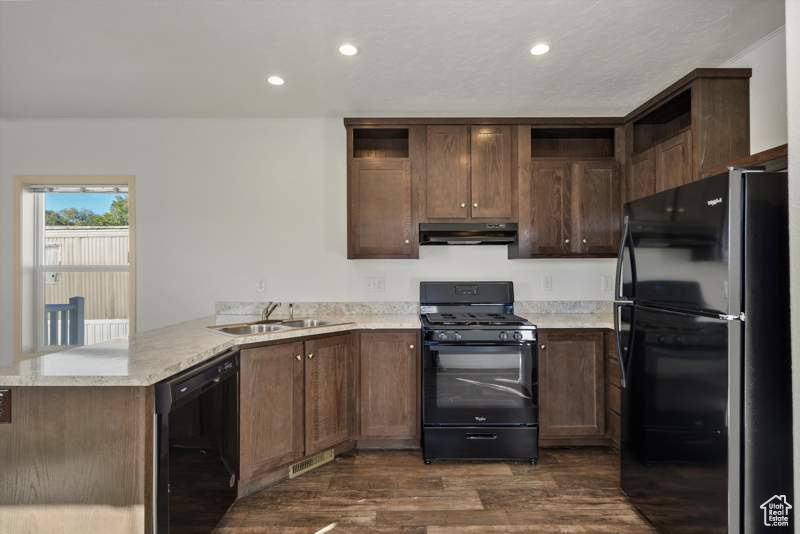 Kitchen with black appliances, under cabinet range hood, open shelves, a peninsula, and dark wood-style floors