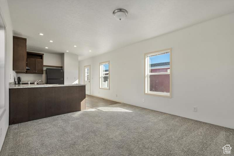 Kitchen with fridge, dark brown cabinetry, light carpet, light countertops, and recessed lighting