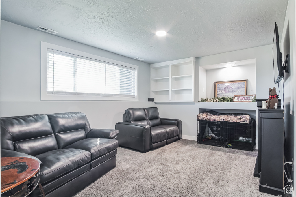 Carpeted living room featuring a textured ceiling, a fireplace, and built in shelves