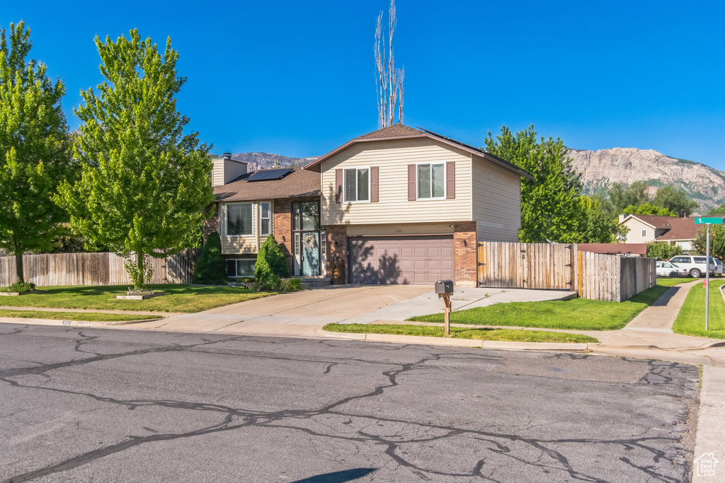 Split level home with a mountain view, solar panels, brick siding, an attached garage, and driveway