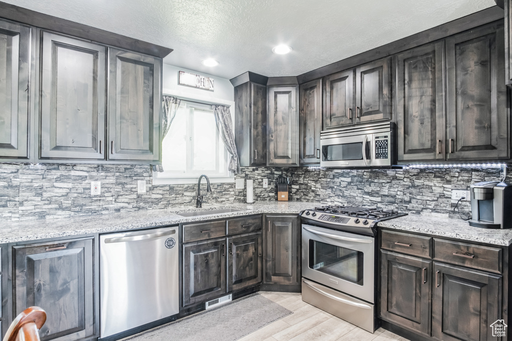 Kitchen with appliances with stainless steel finishes, tasteful backsplash, light wood finished floors, light stone counters, and a textured ceiling