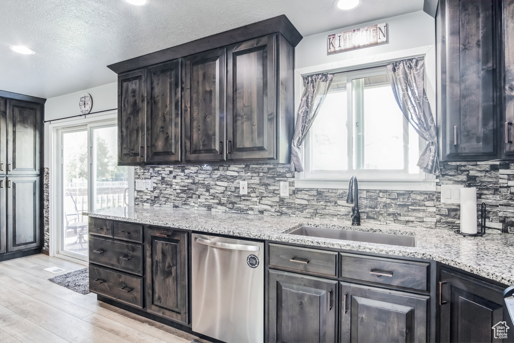 Kitchen with stainless steel dishwasher, light wood finished floors, tasteful backsplash, light stone counters, and a textured ceiling
