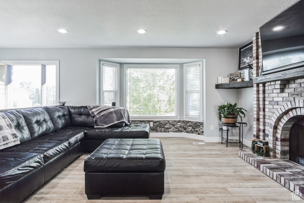 Living area featuring a brick fireplace, wood finished floors, recessed lighting, and a textured ceiling