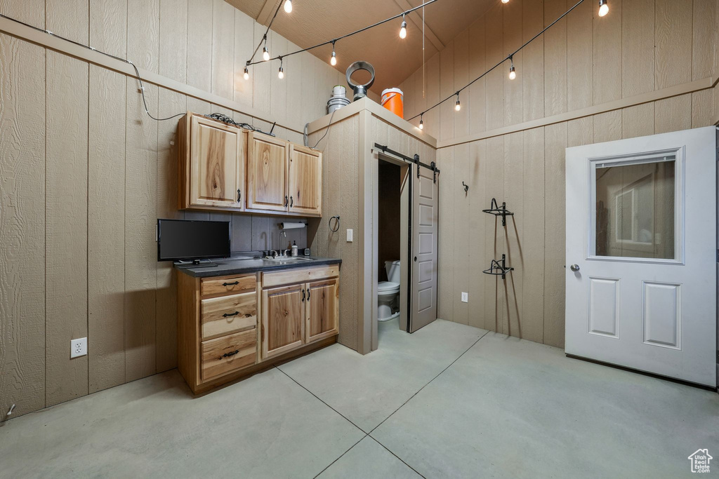 Kitchen with a barn door, dark countertops, concrete flooring, wood walls, and a high ceiling