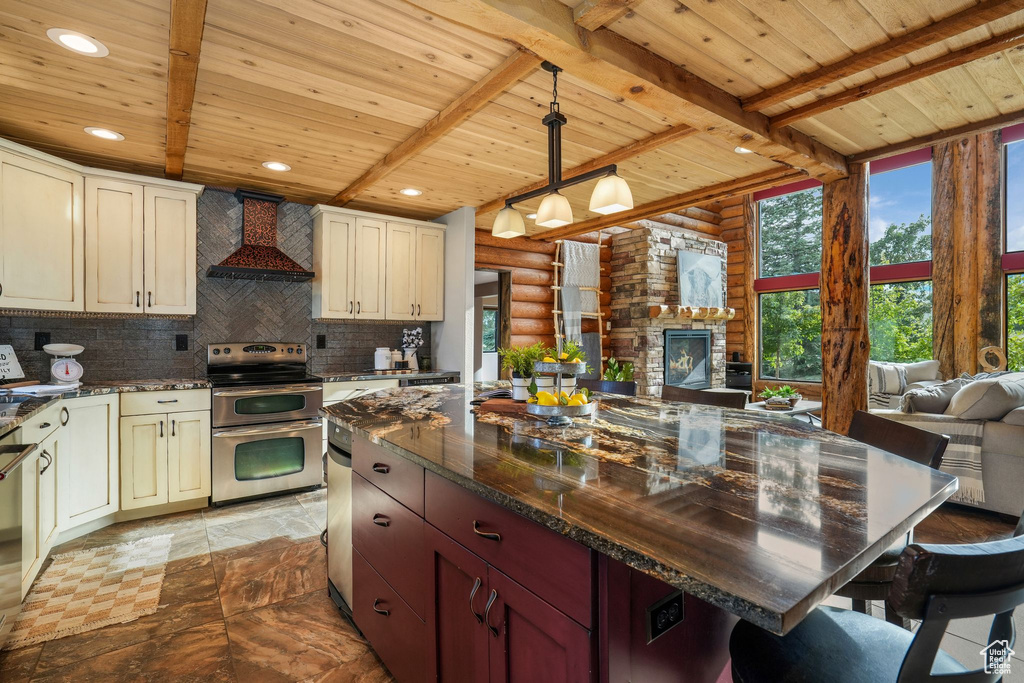 Kitchen featuring wall chimney range hood, double oven range, a wood ceiling with exposed beams, rustic walls, and open floor plan