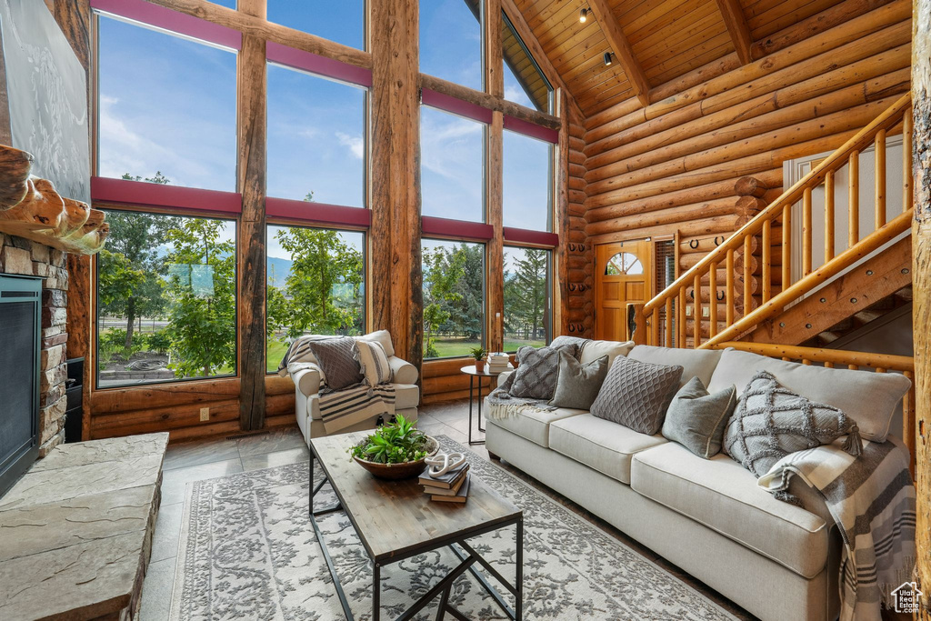 Living area with high vaulted ceiling, a wooden ceiling with exposed beams, log walls, and a fireplace