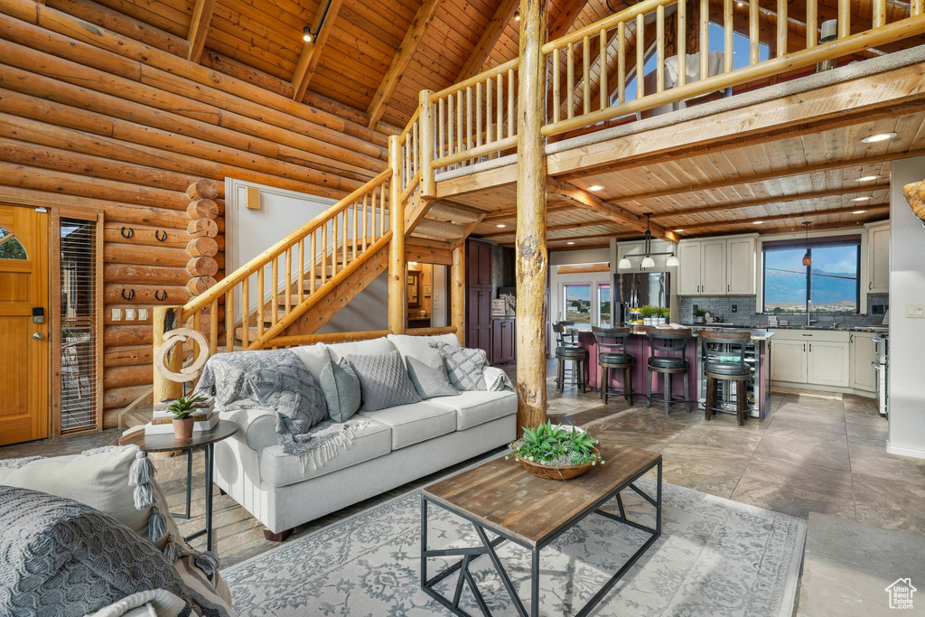 Living room featuring a wood ceiling with exposed beams, a towering ceiling, stairs, and log walls