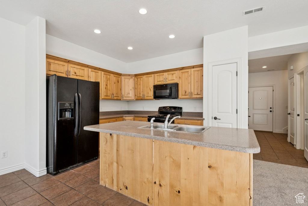 Kitchen with black appliances, dark tile patterned flooring, recessed lighting, an island with sink, and light countertops