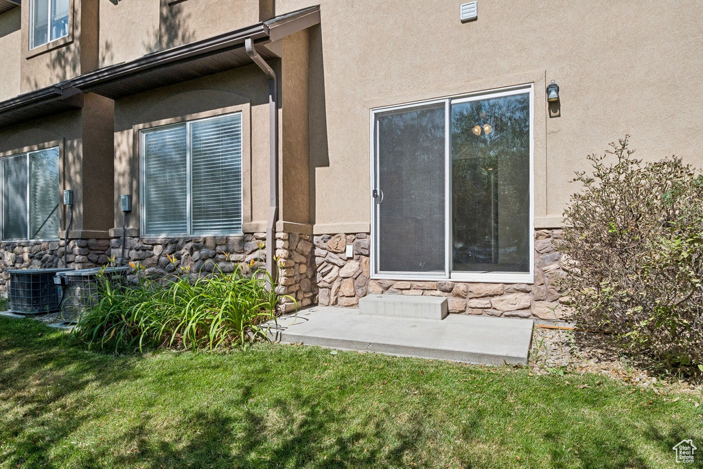 View of exterior entry with stone siding, a yard, and stucco siding