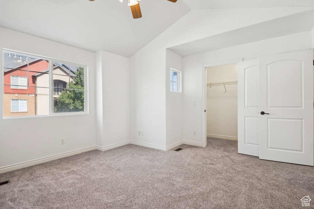 Unfurnished bedroom featuring carpet, vaulted ceiling, ceiling fan, a spacious closet, and a closet