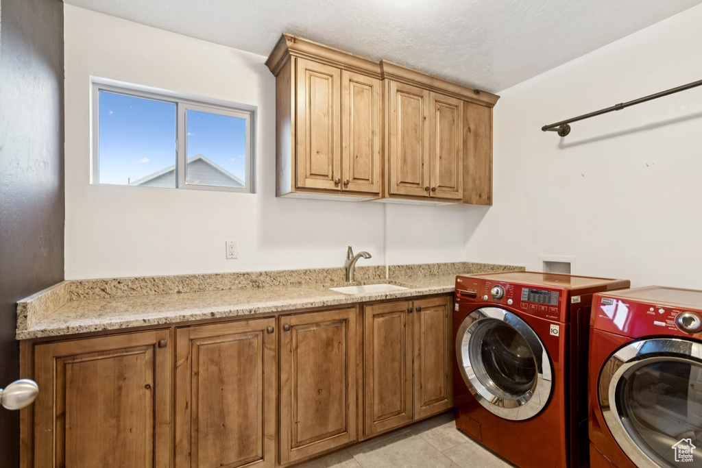 Washroom featuring washing machine and clothes dryer, cabinet space, and light tile patterned floors