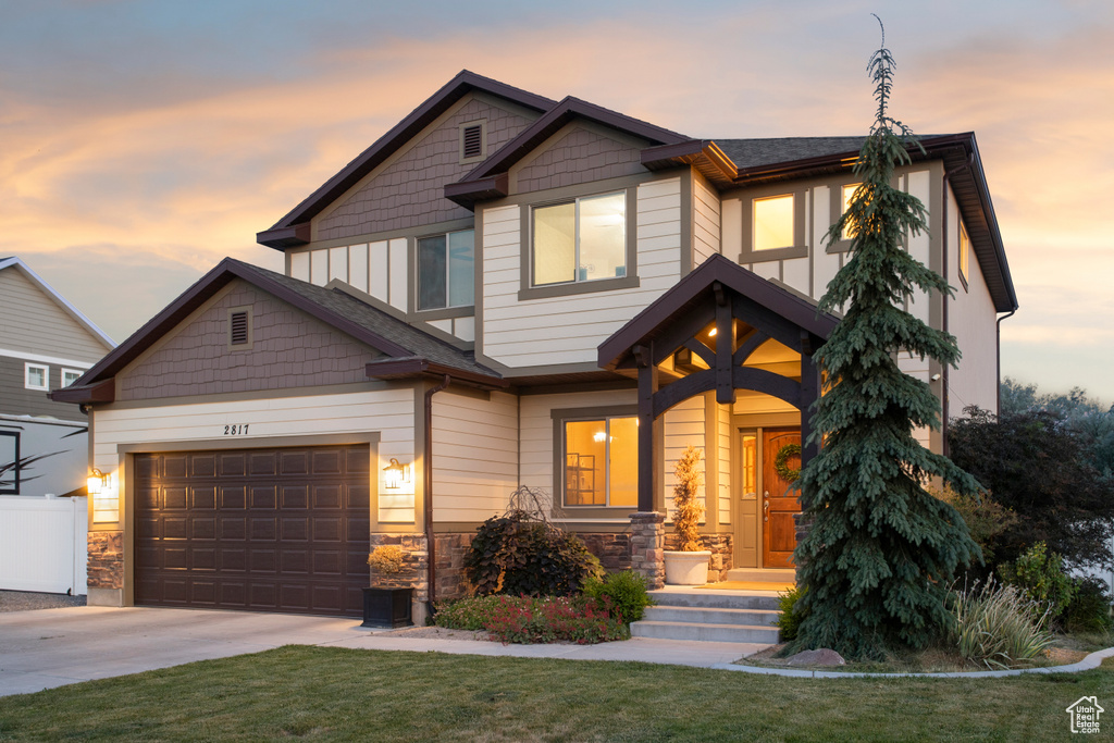 Craftsman-style house featuring driveway, stone siding, a front yard, and an attached garage