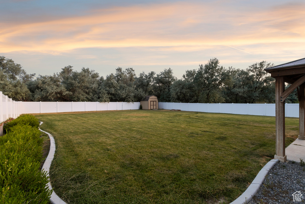 Yard at dusk featuring a storage unit, a fenced backyard, and view of wooded area
