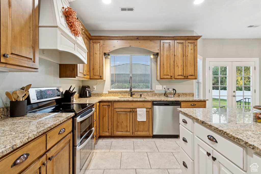 Kitchen with appliances with stainless steel finishes, premium range hood, healthy amount of natural light, light stone countertops, and recessed lighting