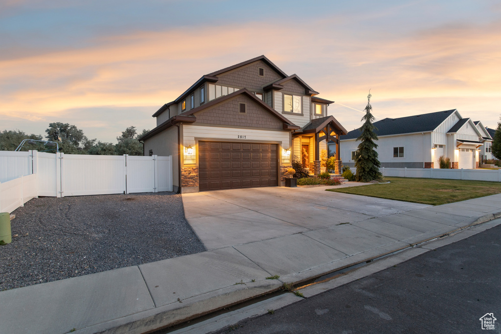 View of front of house featuring an attached garage, concrete driveway, stone siding, and a gate