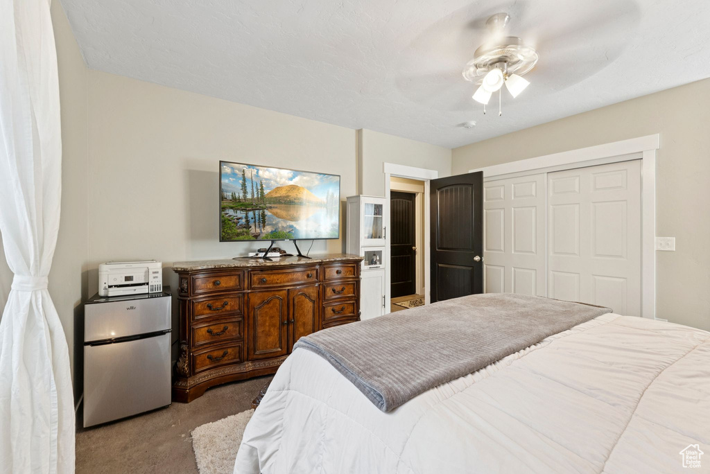 Carpeted bedroom featuring fridge, a closet, and ceiling fan