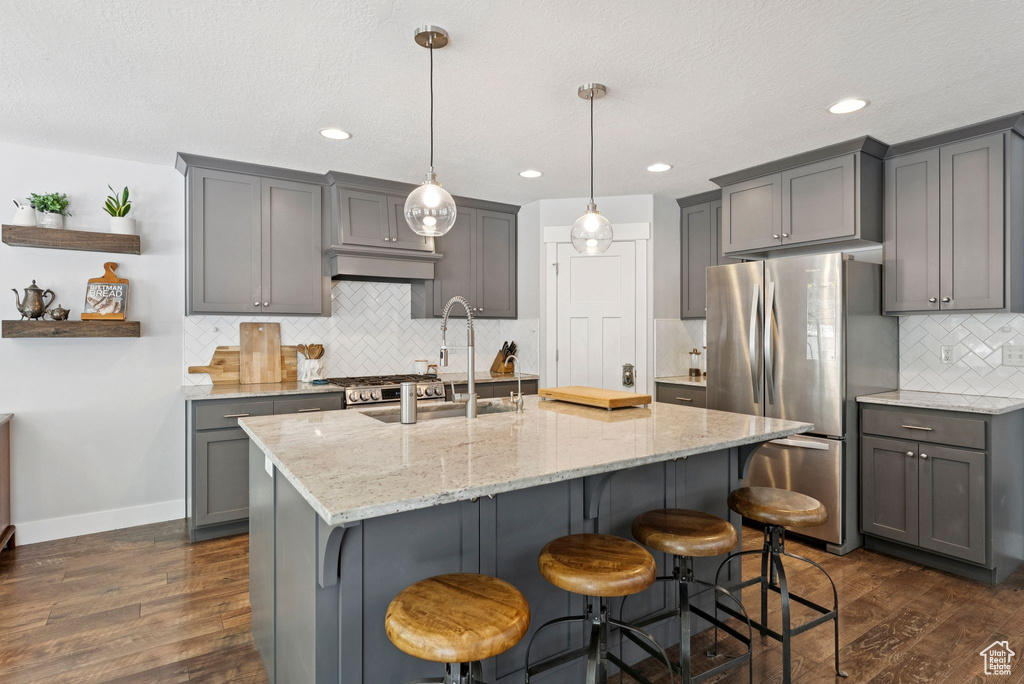 Kitchen featuring freestanding refrigerator, gray cabinetry, dark wood-type flooring, tasteful backsplash, and light stone countertops