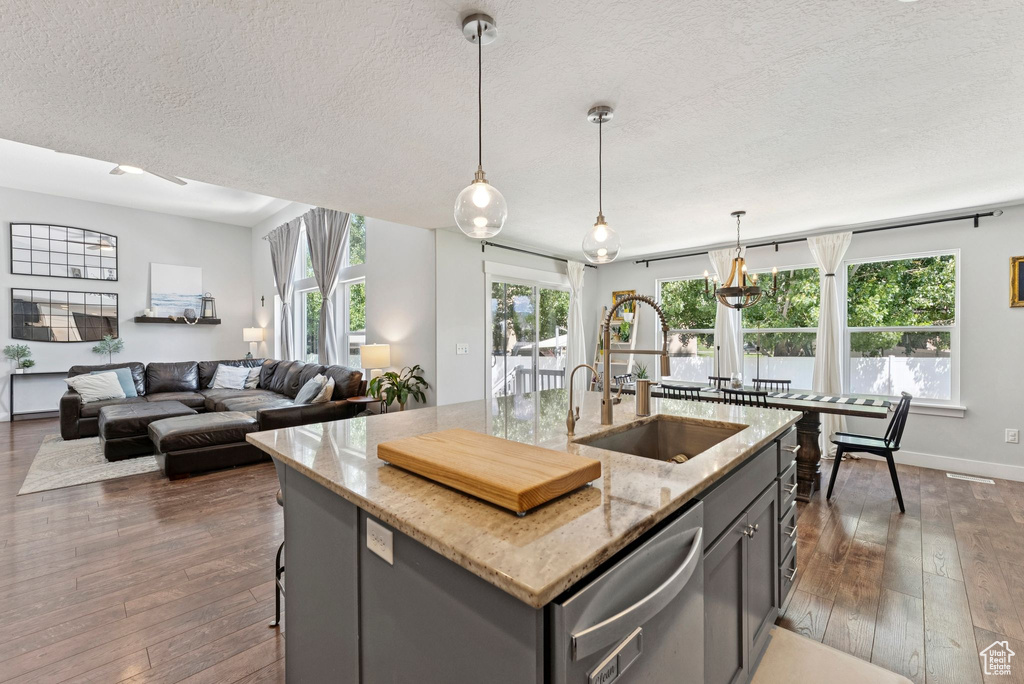 Kitchen featuring dishwasher, a textured ceiling, dark wood-style flooring, light stone countertops, and a kitchen island with sink